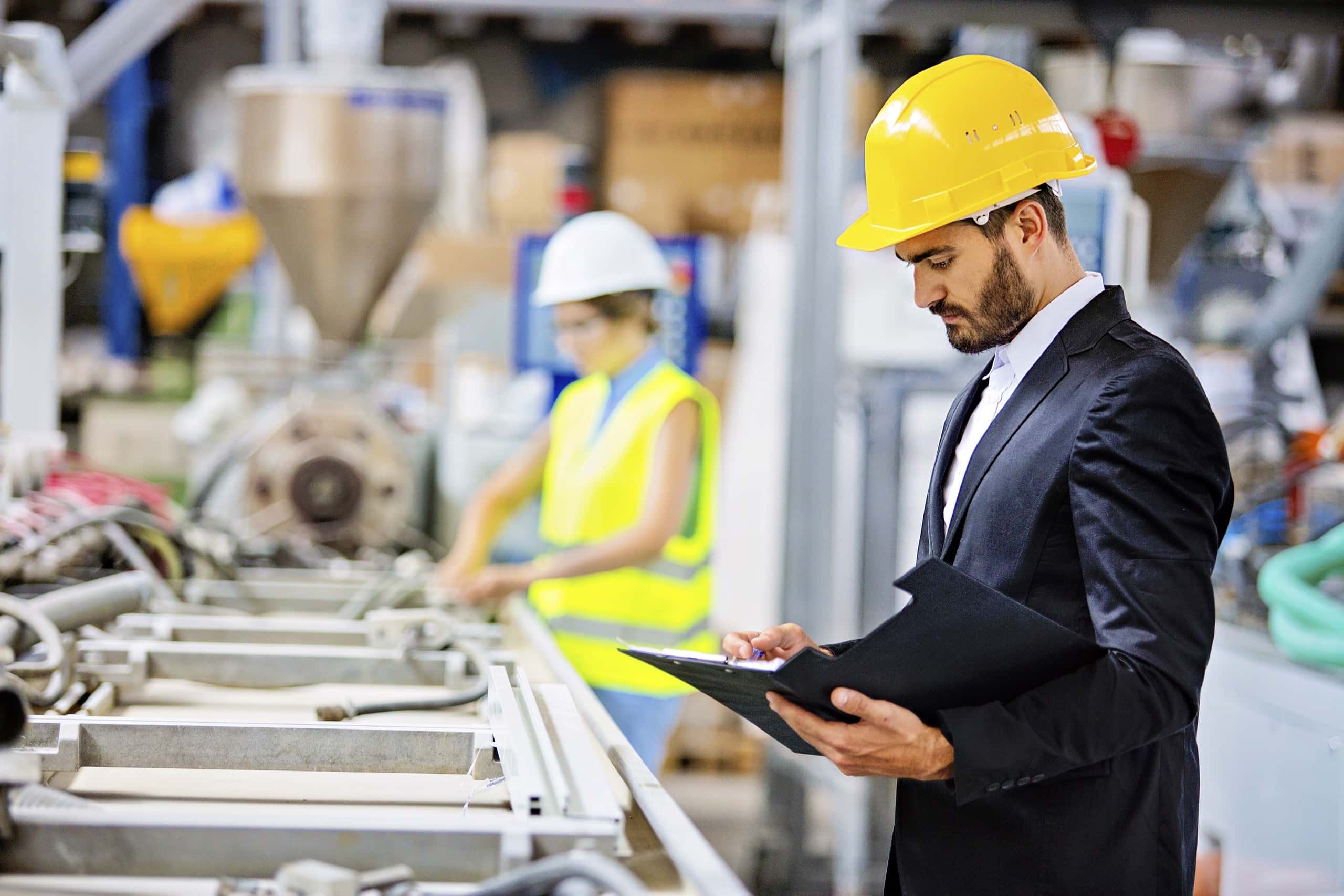 A manufacturing professional wearing a hard hat and safety glasses reviews a clipboard in front of an industrial machine, symbolizing the focus on production and innovation enabled by Fast Fixx''s reliable IT solutions.