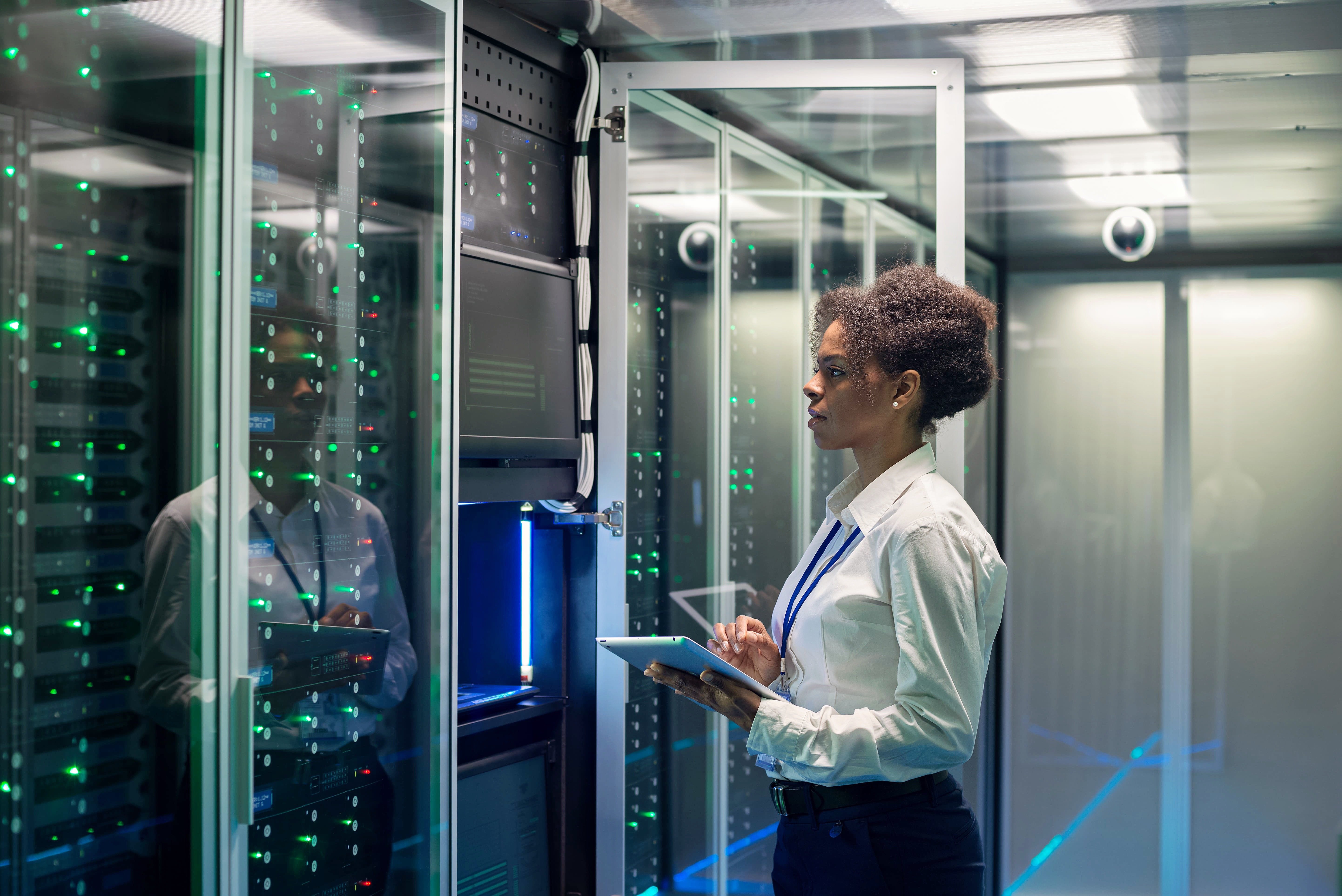 A female IT professional inspecting servers in a data center while using a tablet, representing the importance of disaster recovery testing to guarantee a smooth and rapid recovery in case of disruptions