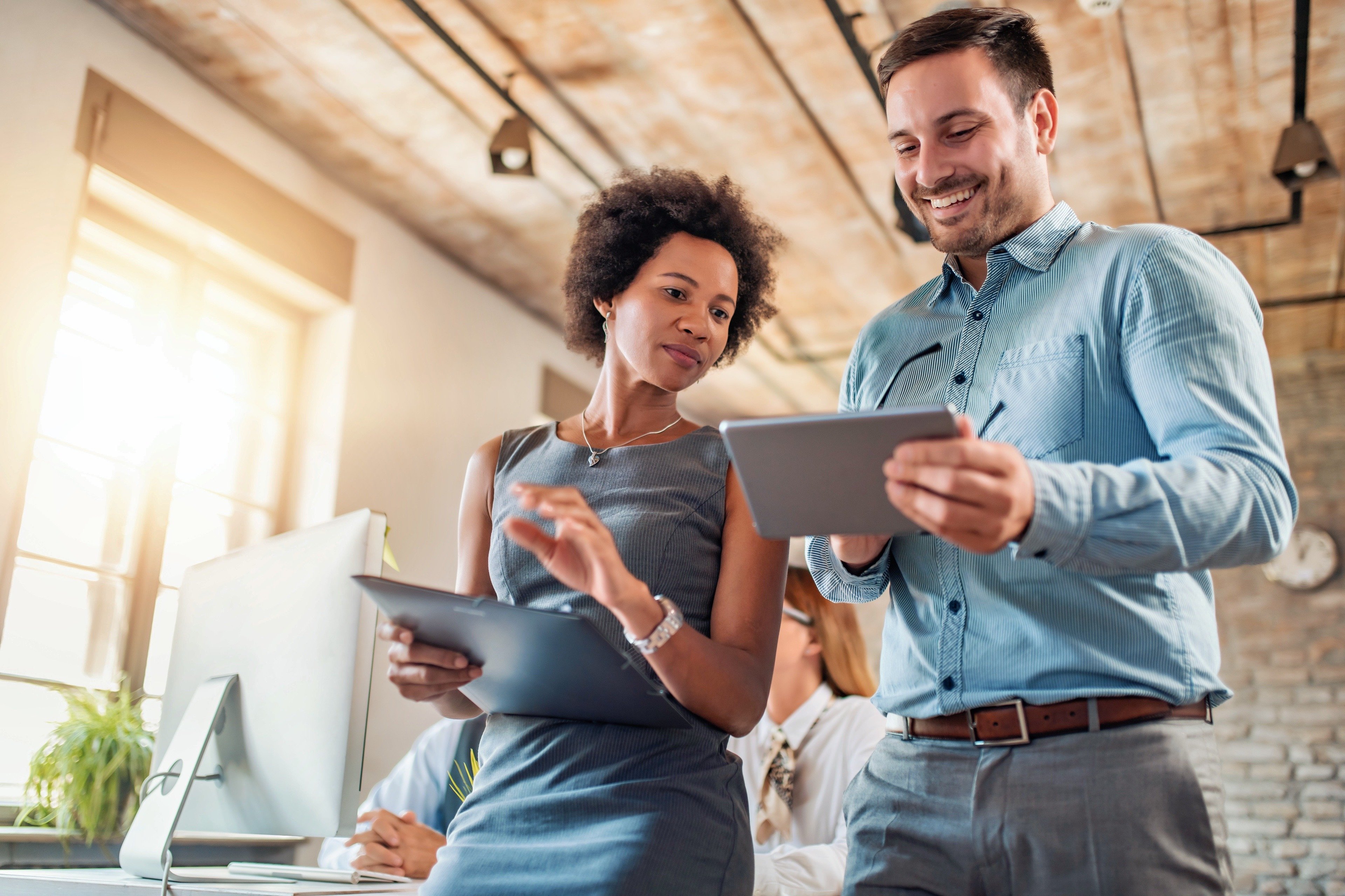 A smiling businessperson holds a tablet while discussing wireless network design and implementation with a colleague, representing Fast Fixx's expertise in providing secure and reliable wireless network solutions for offices and campuses.