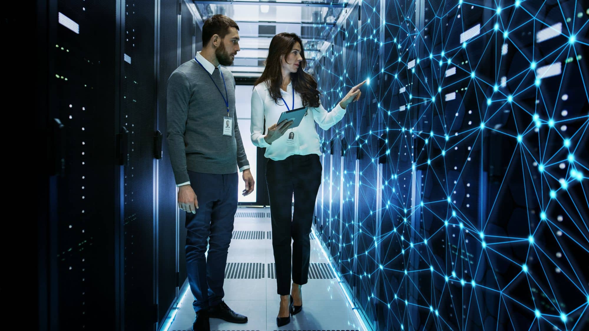 A man and a woman in a datacenter, pointing at lines on the wall representing a firewall