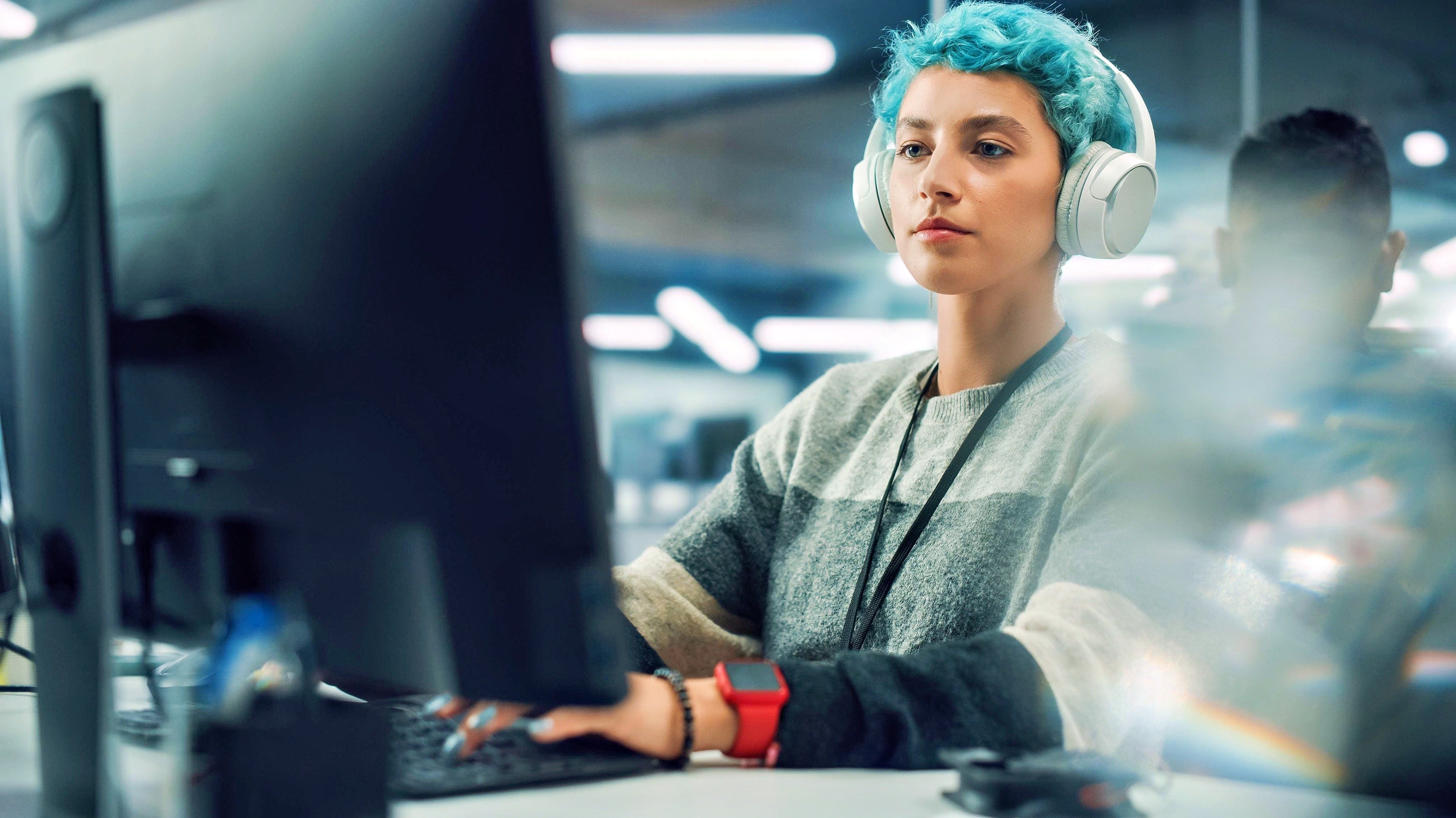 A young woman wearing headphones and working on a computer in an office, representing the cloud application development and deployment services offered by Fast Fixx to build and deploy cloud-native apps quickly and efficiently