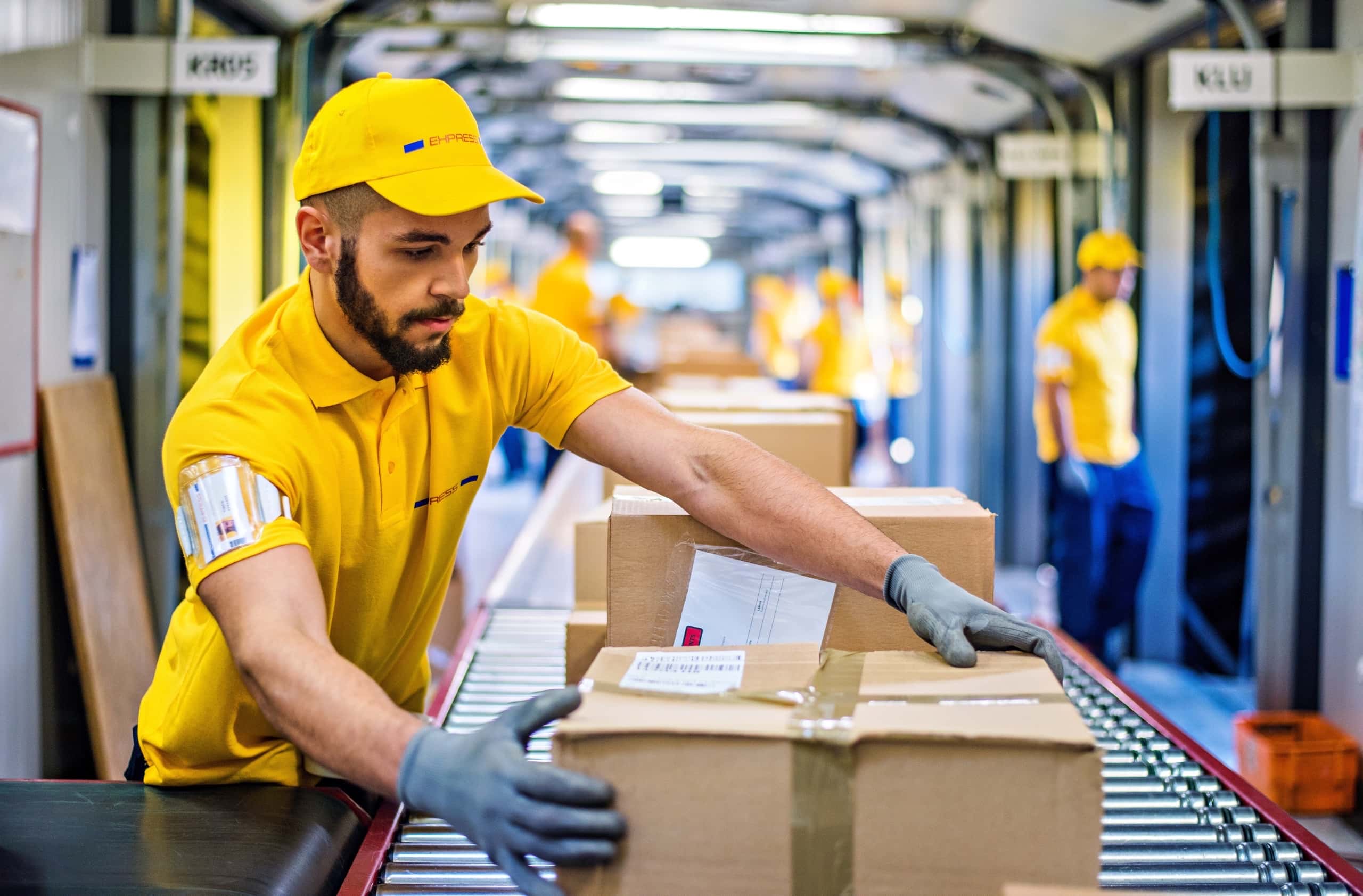 A worker in a yellow uniform is pushing a box along a conveyor belt in a warehouse, representing the tailored IT solutions offered by Fast Fixx for the logistics industry