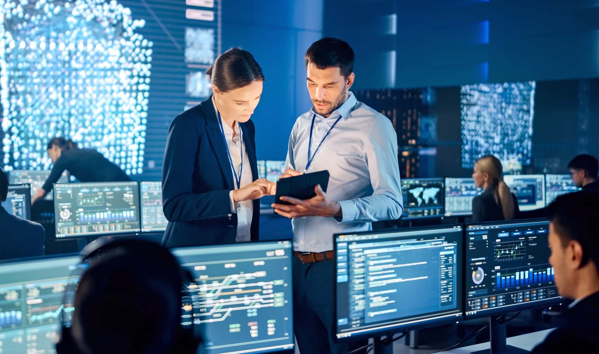 IT professionals discussing cloud security while looking at a tablet in a data center, representing the proactive cloud threat detection and response services offered to protect cloud environments.