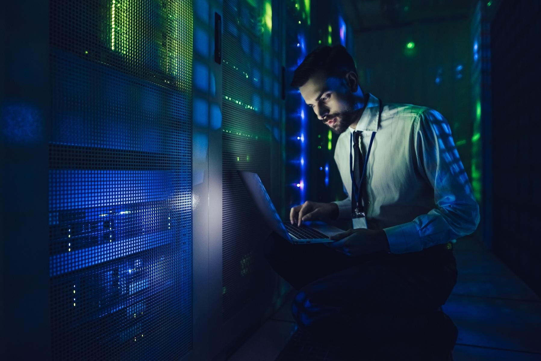 IT professional working on a laptop in a data center with rows of servers, representing the 24/7 threat protection and response services offered by Fast Fixx's managed threat response solution