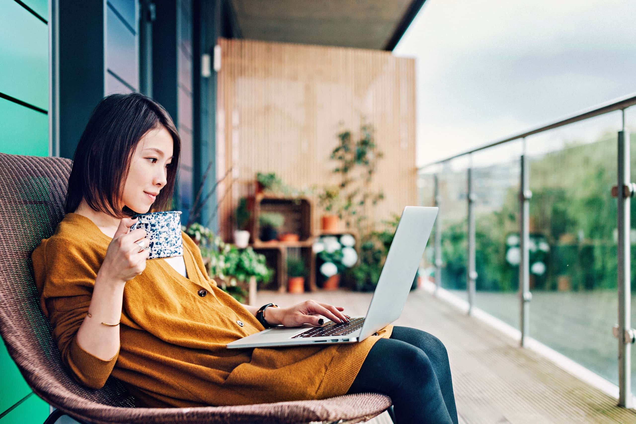 A woman working remotely on her laptop while enjoying a cup of coffee on her balcony, which relates to the text by illustrating the concept of secure remote wor